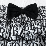 Black and white patterned baby romper with a black bow on a textured white background